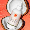 A ProductPhoto of RootCleanse: the best moisturizing shampoo for natural hair care. The bottle is posed inside of a coconut, one of the food-grade, natural ingredients included in the formula.