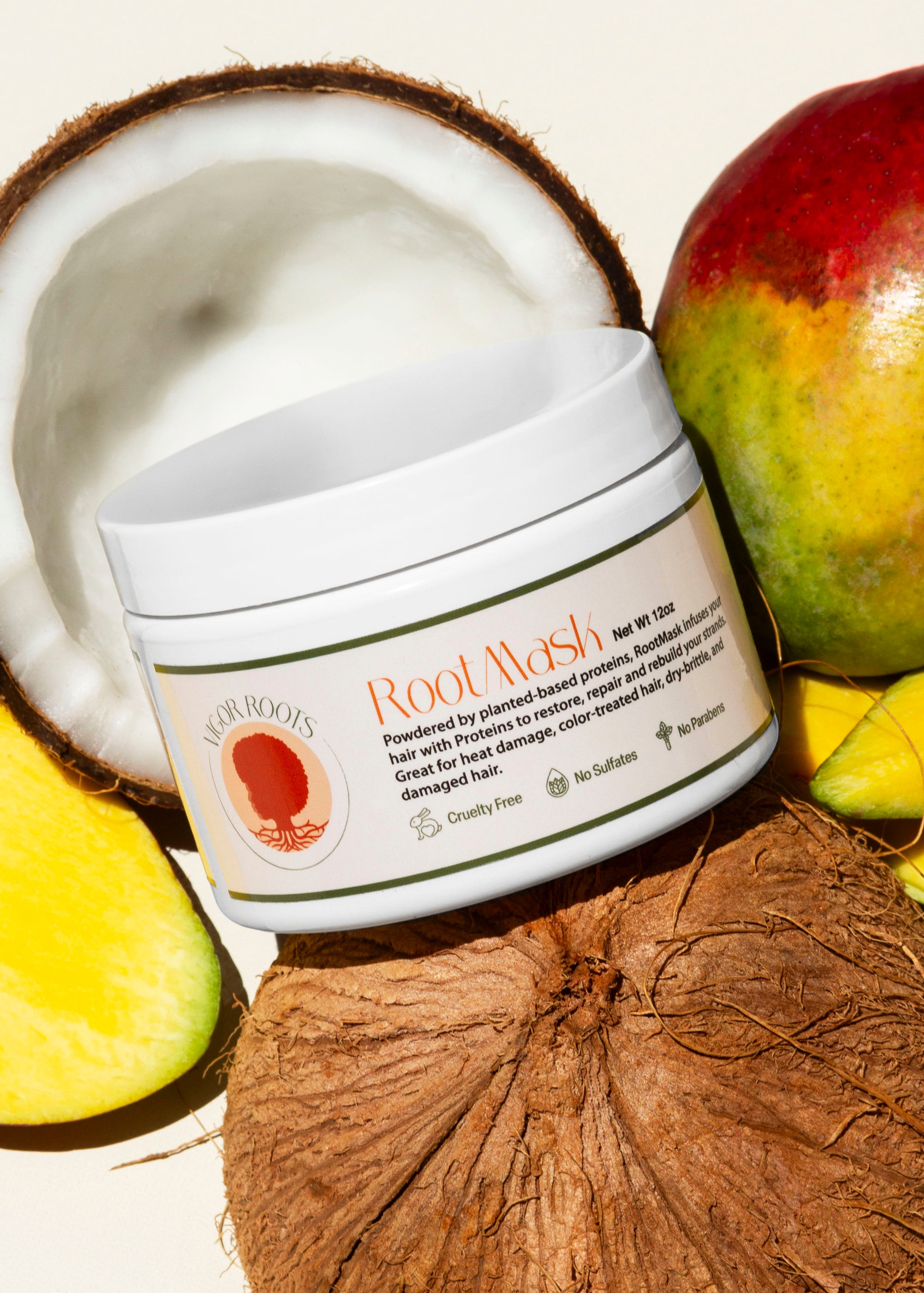 A jar of RootMask- Vigor Roots' reparative hair mask is posed with fresh coconut & mango- some of the food-grade, all natural ingredients featured in the luxurious formula.